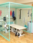 Wnętrze domu pomocy. Gabinet rehabilitacji. Stół rehabilitacyjny stojący w turkusowej klatce rehabilitacyjnej. Na podłodze drewniany parkiet ułożony w jodełkę